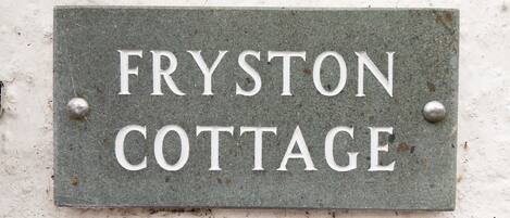 Ein Metallschild mit dem Schriftzug "FRYSTON COTTAGE" an einer Wand befestigt.