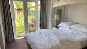 Een slaapkamer met een bed, een nachtkastje, een lamp en uitzicht op een tuin door een schuifdeur.