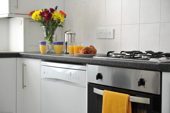 A modern kitchen with white cabinets, a gas stove, a coffee maker, and a vase with flowers.