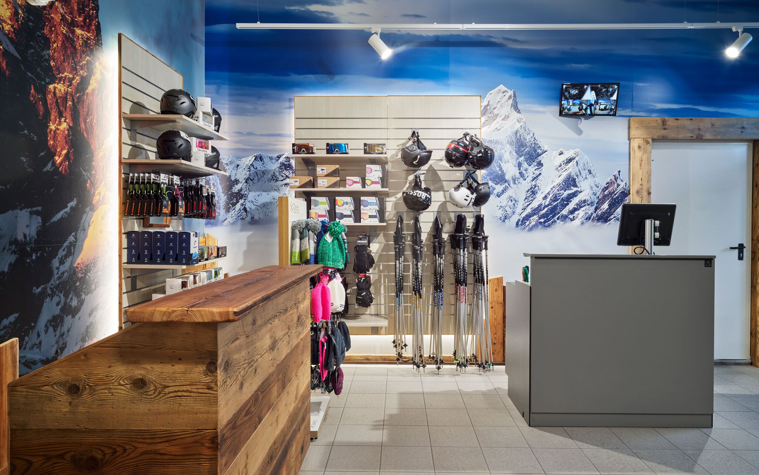 A ski equipment store with wooden shelves, a reception desk, and a wall mural of a mountain landscape.