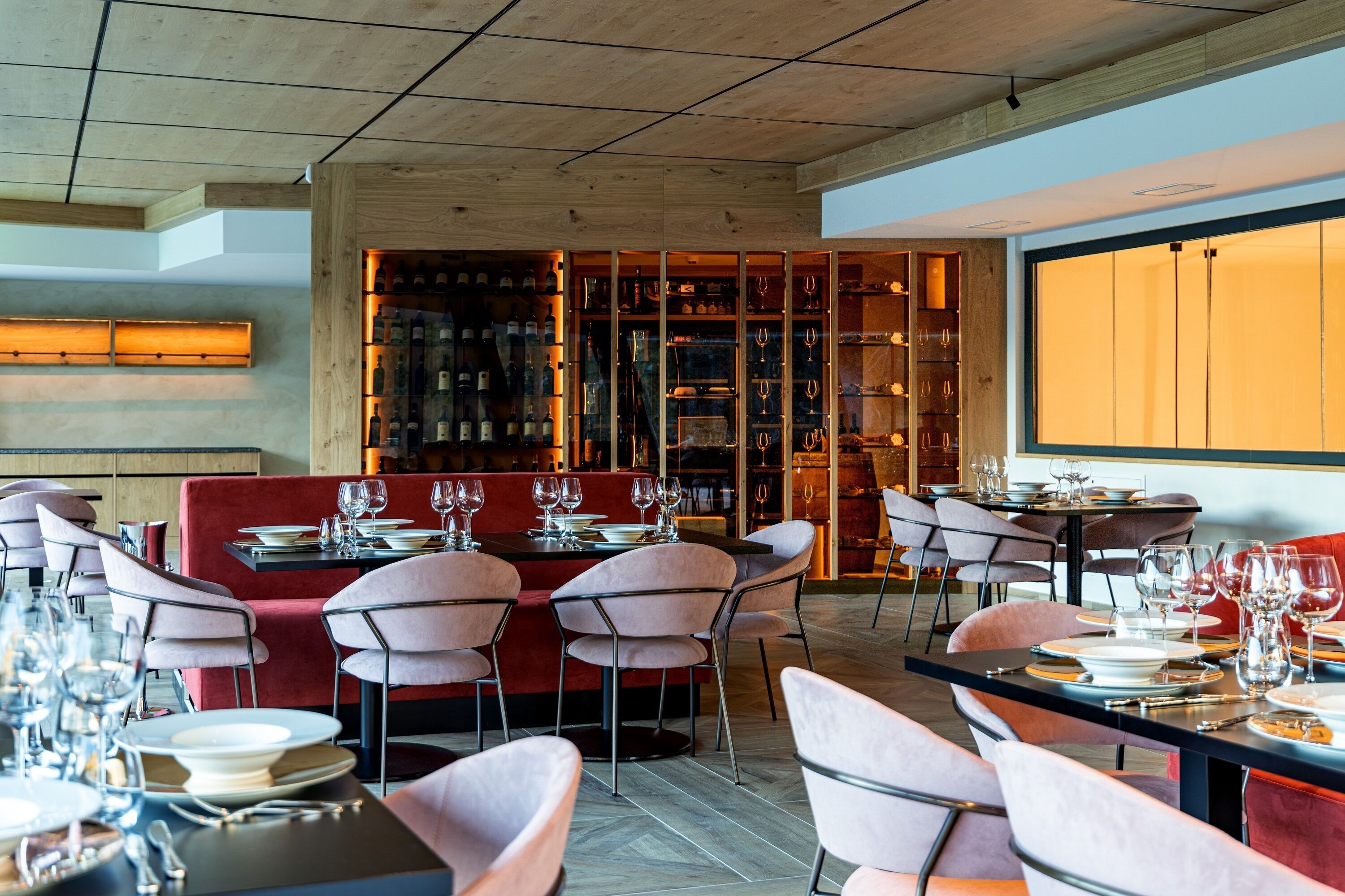 A modern restaurant interior with wooden ceiling, red seating, and a wine display.