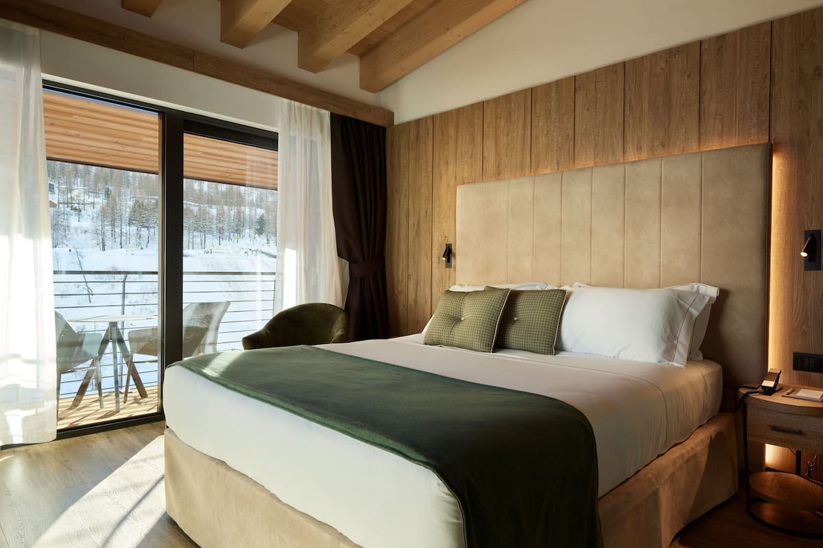 Quarto com cama grande, cabeceira de madeira e vista para uma paisagem nevada através de uma porta de correr.