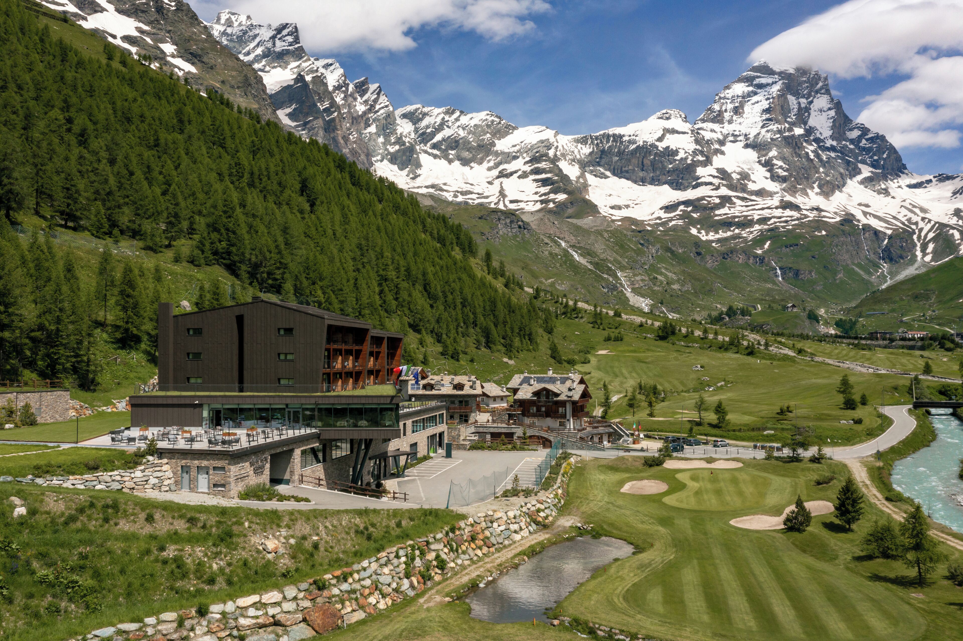 Un hotel moderno con facciata in vetro, terrazza sul tetto e vista sulle montagne innevate.