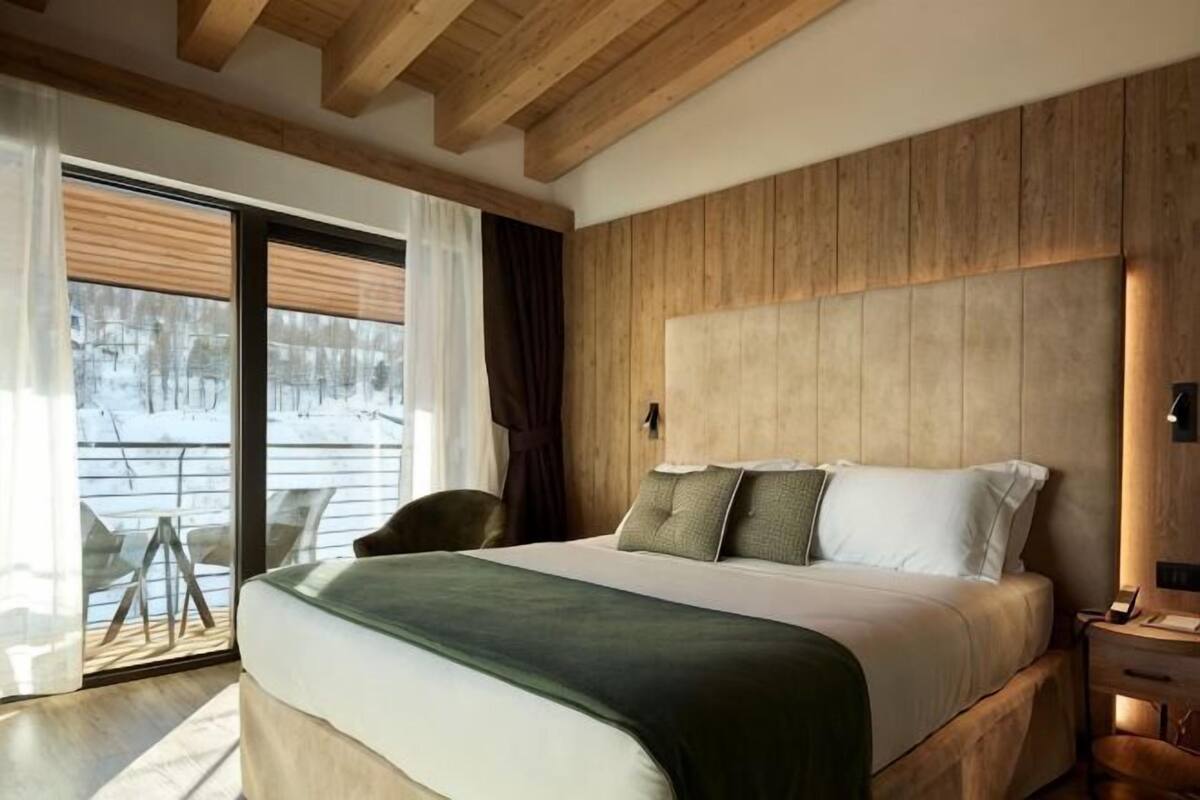 Quarto com cama grande, cabeceira de madeira e vista para uma área externa coberta de neve.