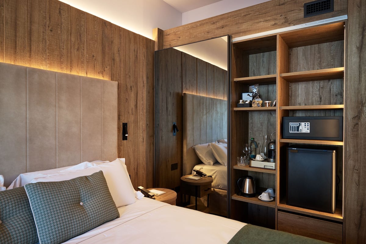 Quarto de hotel com cama, mesa de cabeceira e minibar embutido, incluindo máquina de café e outros serviços.