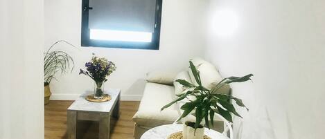 Un petit salon moderne, comprenant un canapé, une table basse et deux plantes en pot.