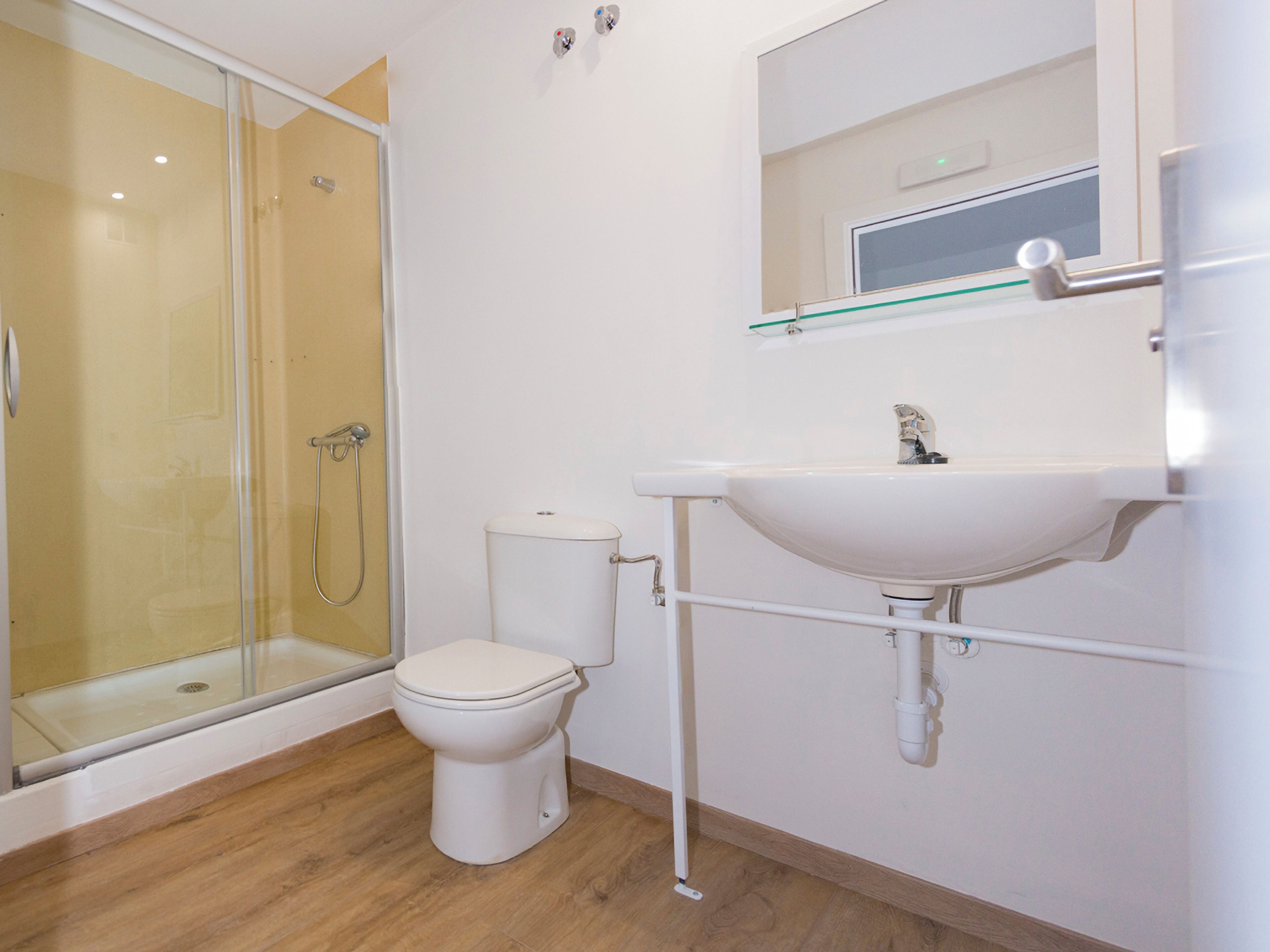 A bathroom with a glass shower enclosure, a toilet, and a sink with a mirror above it.