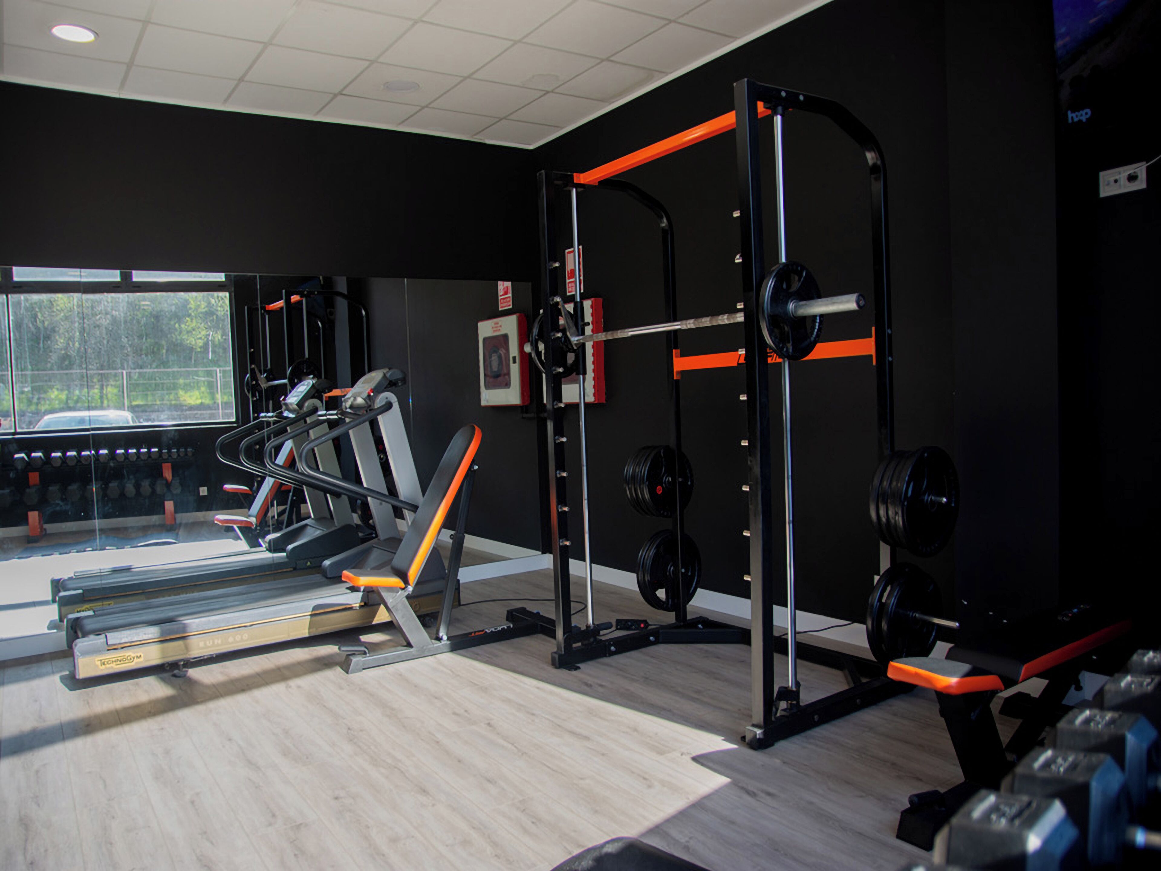 Un gimnasio con equipo de ejercicio, un rack de pesas y un ventanal con vistas a árboles.