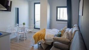 Une chambre moderne avec un lit, un canapé, un bureau et une chaise. Il y a une fenêtre avec des rideaux et une vue sur l’extérieur.