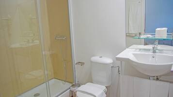 Un baño moderno con cabina de ducha de vidrio, inodoro blanco y lavamanos con repisa de vidrio arriba.