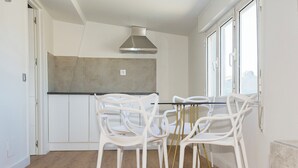 Une cuisine moderne avec des armoires blanches, une hotte de cuisinière en acier inoxydable et un coin repas avec des chaises blanches et un pied de table doré.