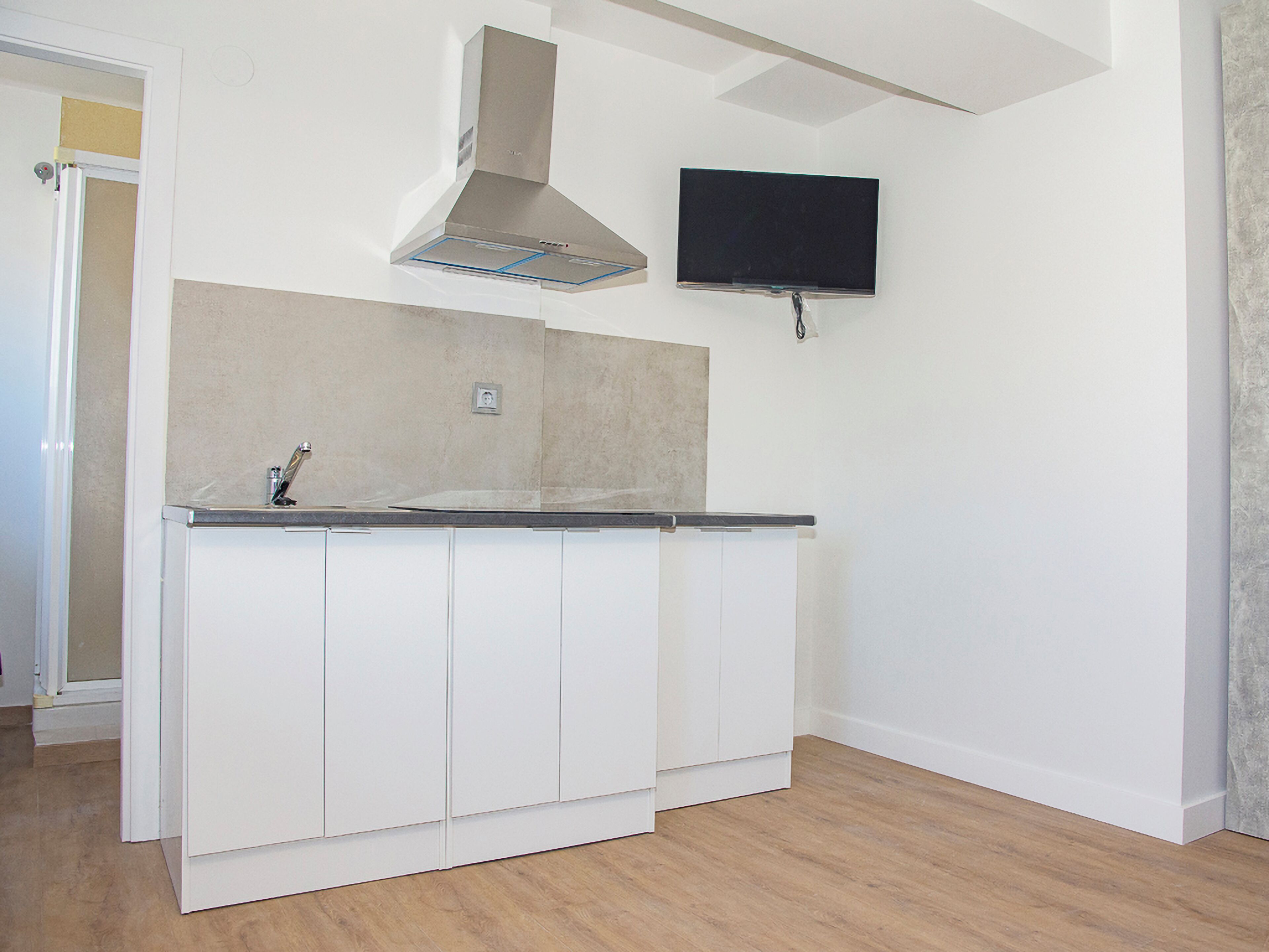 Una cocina con armarios blancos, una campana extractora de acero inoxidable y un televisor de pantalla plana montado en la pared.