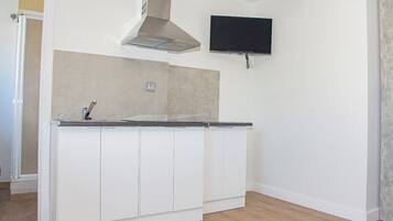 Una cocina con armarios blancos, una campana extractora de acero inoxidable y un televisor de pantalla plana montado en la pared.