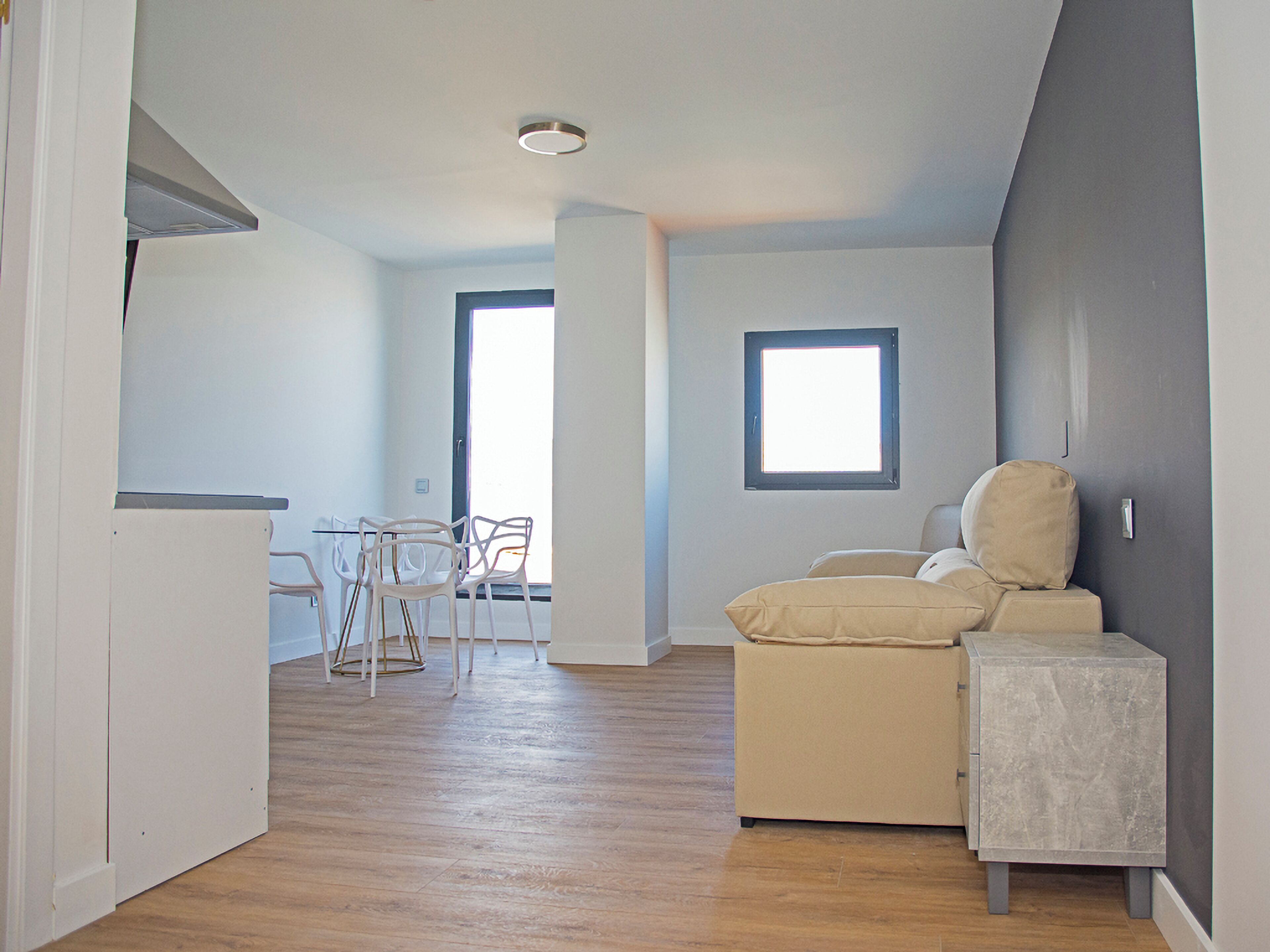 Une pièce avec un plancher en bois, un canapé, une petite table et deux chaises. Il y a une fenêtre et une porte.