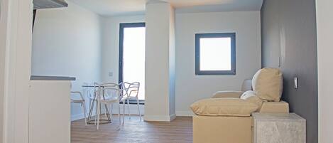 A room with a wooden floor, a sofa, a small table, and two chairs. There is a window and a door.