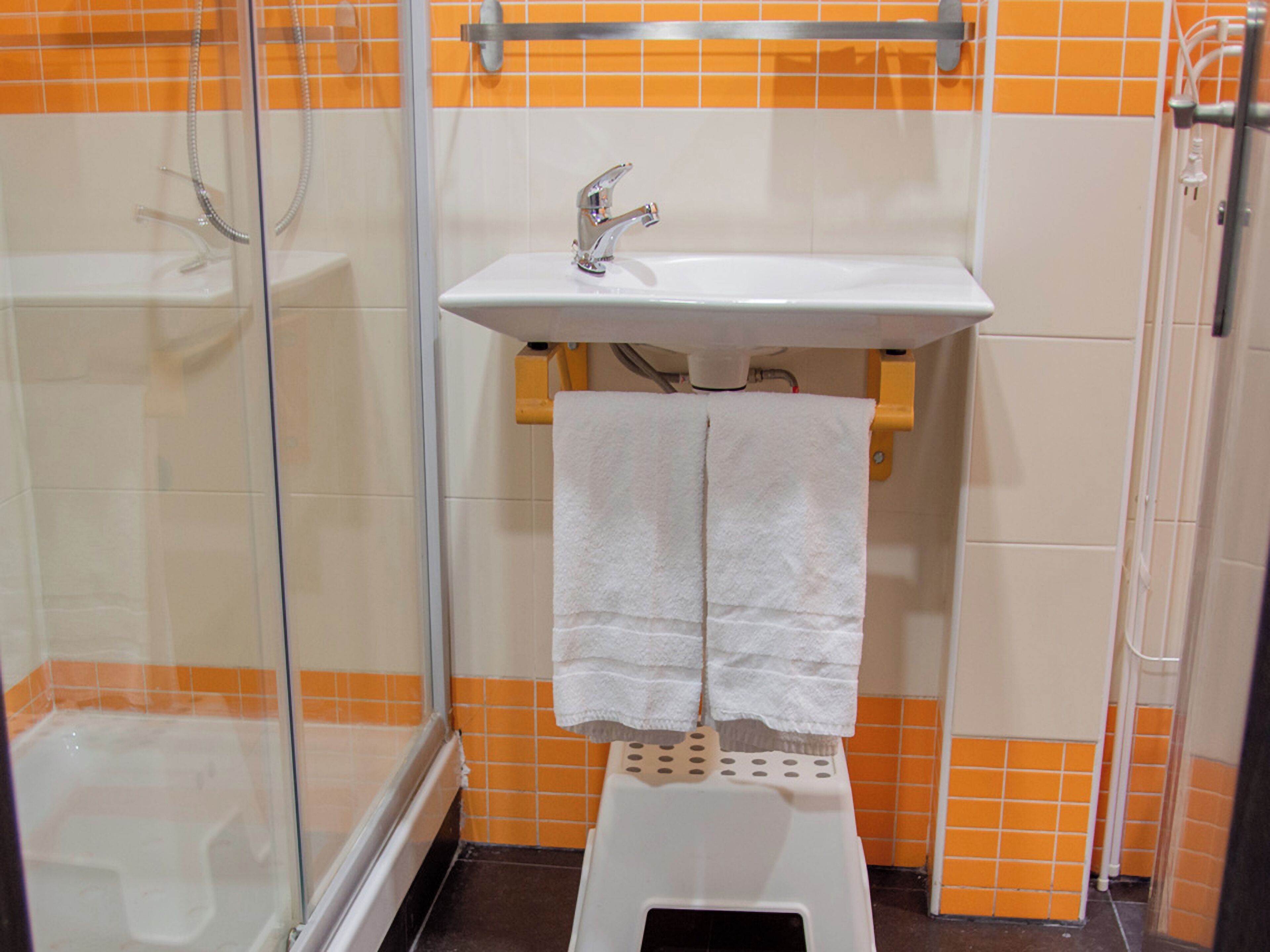Un baño con cabina de ducha de vidrio, un lavabo blanco con grifo cromado y una toalla blanca colgada en un perchero.