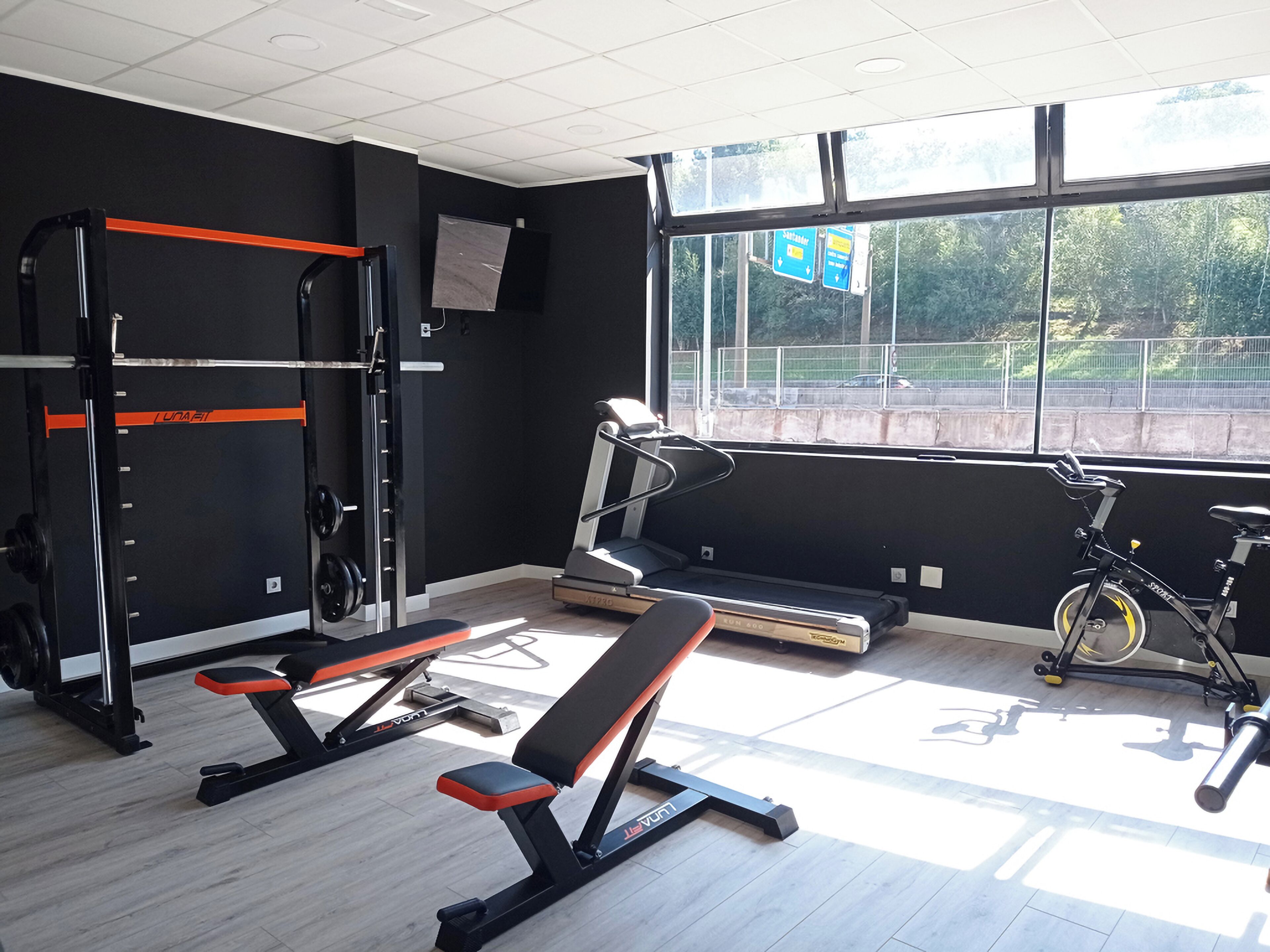 Une salle de sport équipée d’un banc, d’un support à poids, d’un tapis de course et d’un vélo d’appartement.
