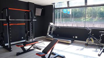 Une salle de sport équipée d’un banc, d’un support à poids, d’un tapis de course et d’un vélo d’appartement.