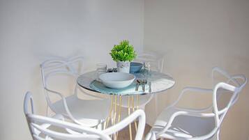 Una mesa redonda con cubierta de vidrio rodeada de sillas blancas. Hay una pequeña planta en maceta sobre la mesa.
