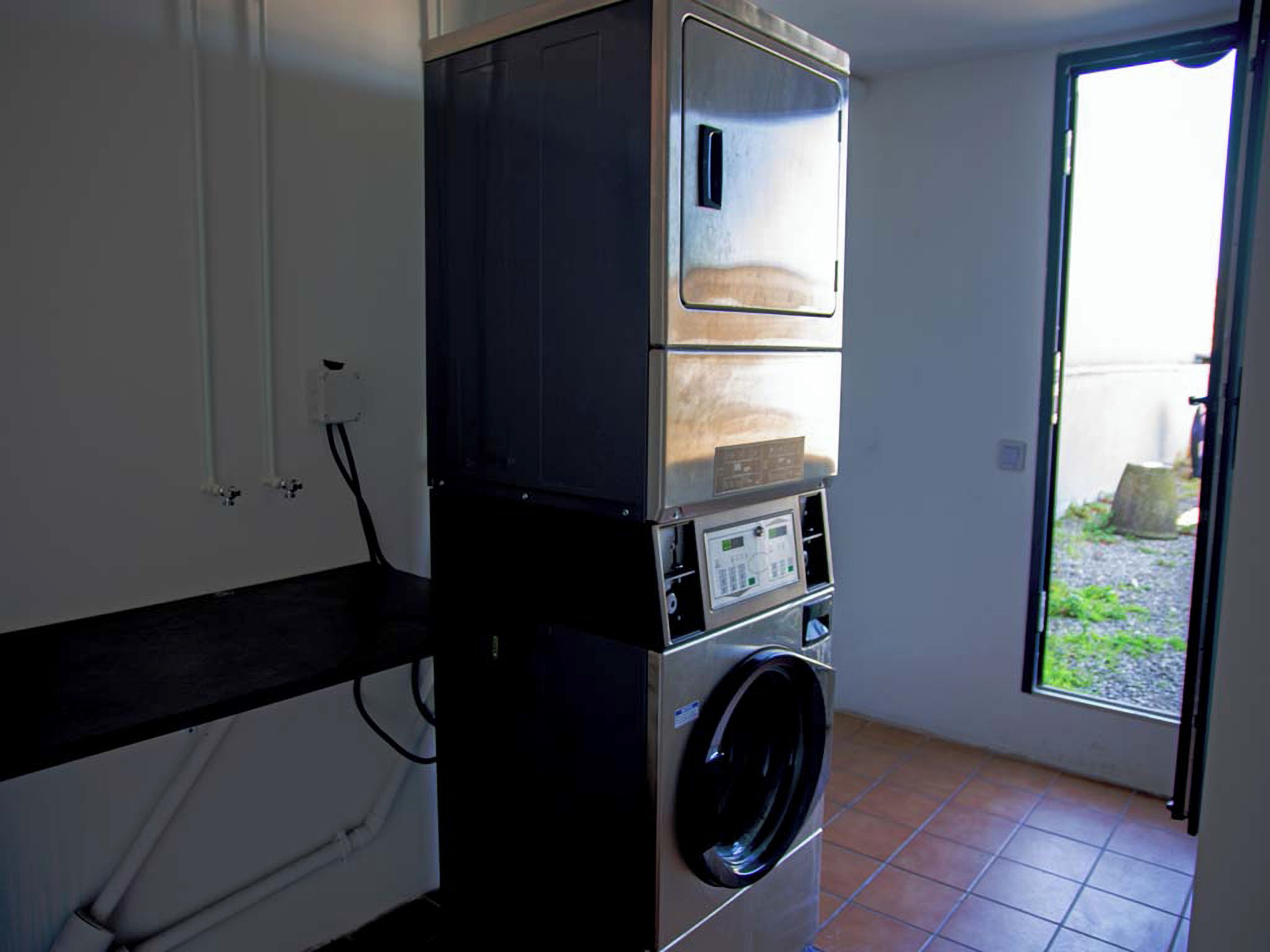 A compact laundry room with a washing machine and dryer stacked on top of each other, a window with a view of the outside, and a door leading to a patio area.