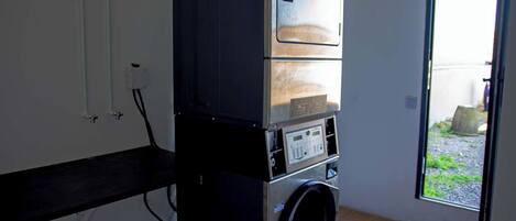 A compact laundry room with a washing machine and dryer stacked on top of each other, a window with a view of the outside, and a door leading to a patio area.