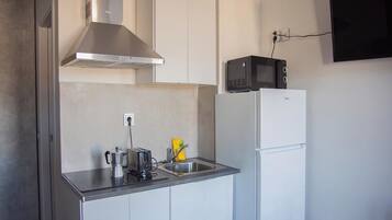 Una cucina compatta con mobili bianchi, una cappa aspirante in acciaio inox, un forno a microonde e un frigorifero bianco.