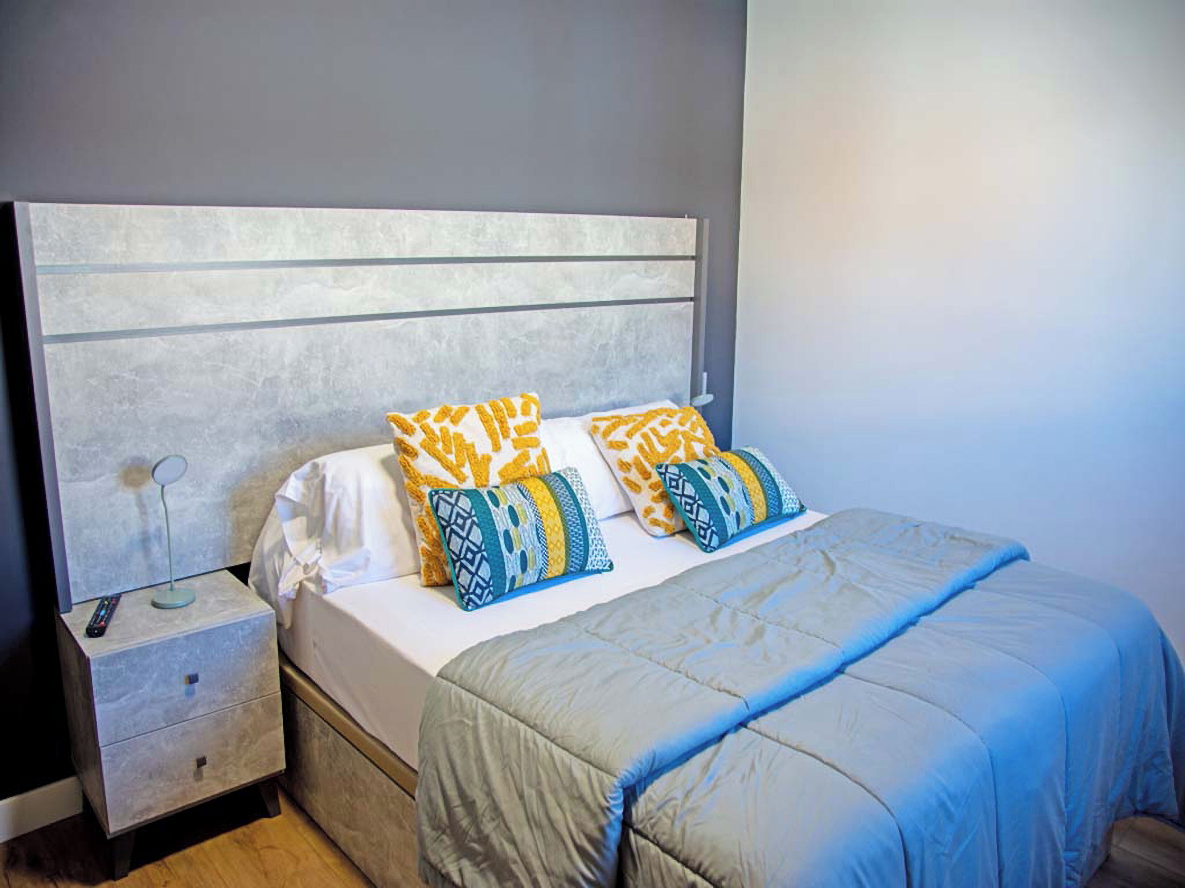 A bedroom with a bed, a nightstand, a lamp, and patterned pillows.
