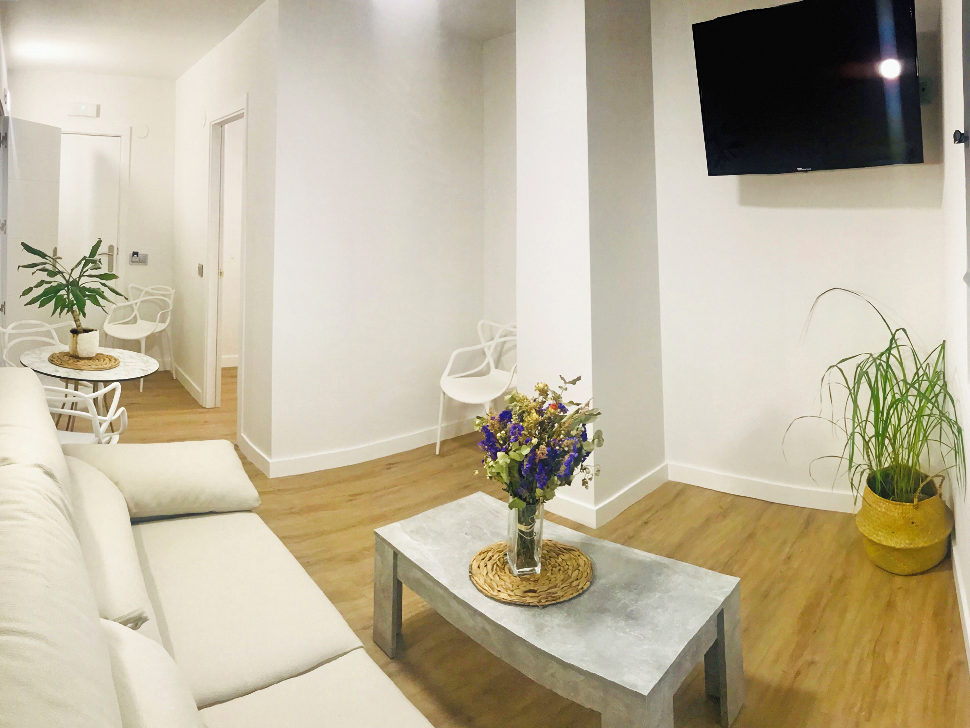 A modern living room with a sofa, a coffee table with a vase of flowers, and a flat-screen TV mounted on the wall.
