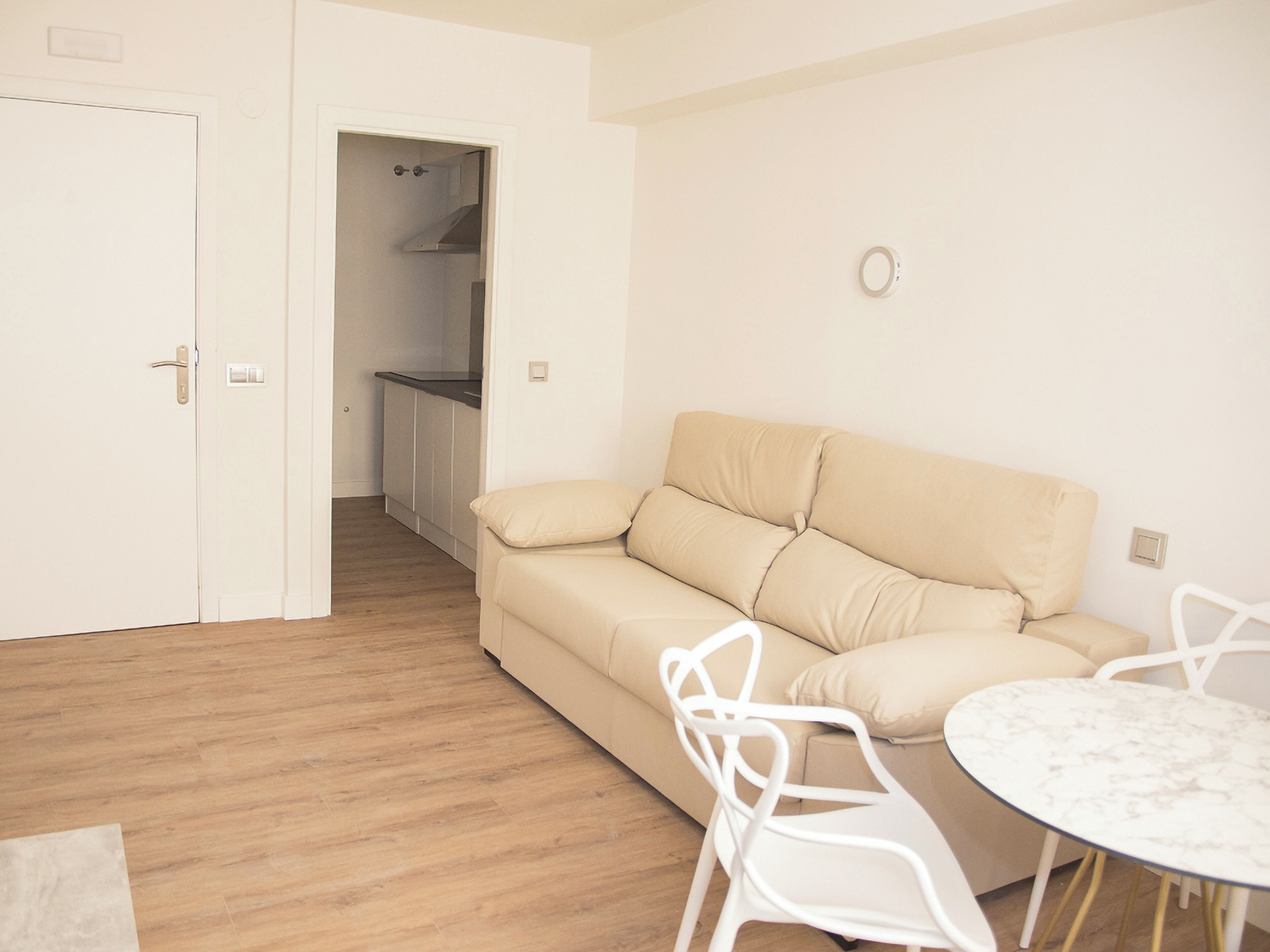 Una sala de estar minimalista con un sofá color beige, una silla blanca y una mesita redonda.