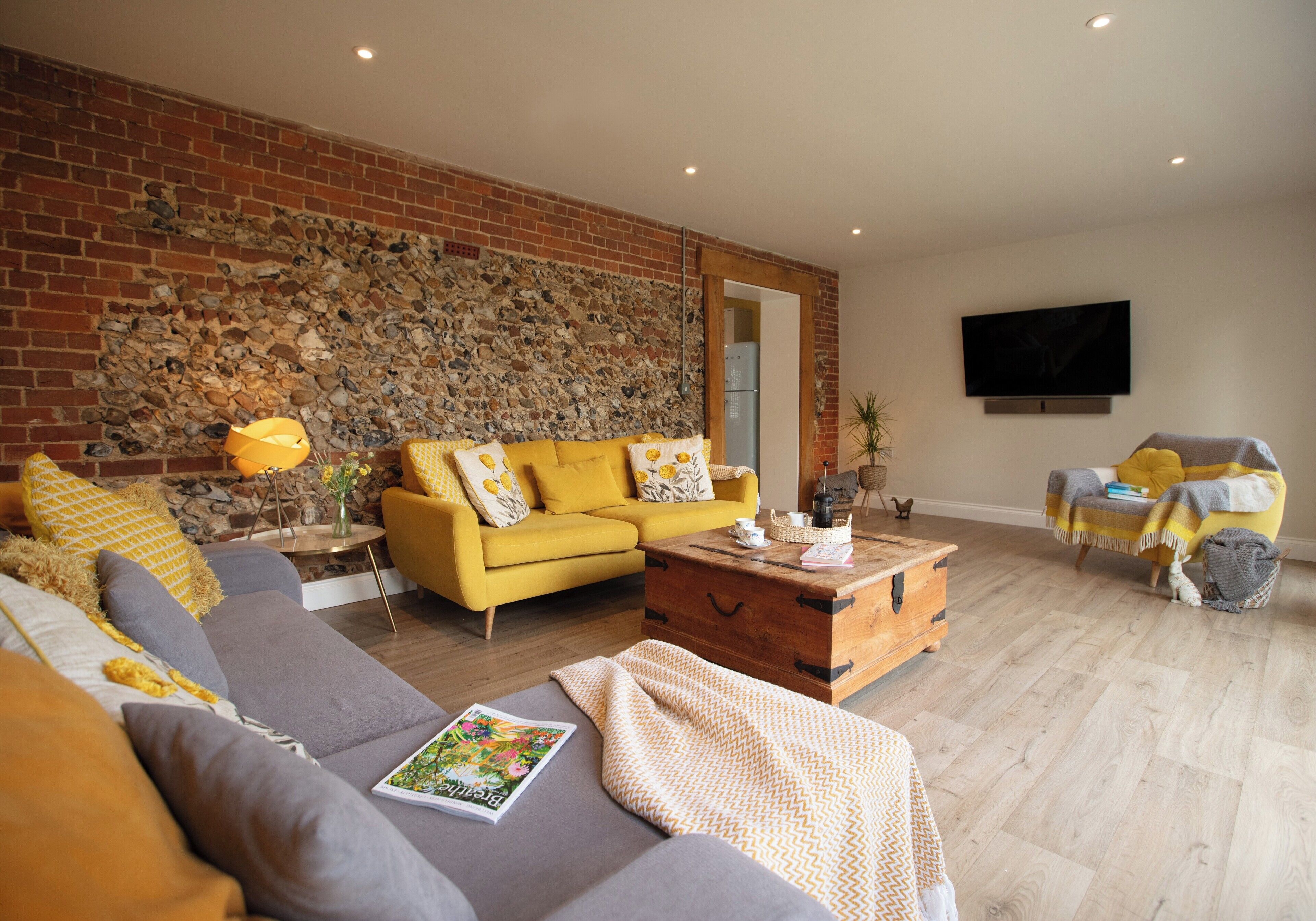 A living room with a yellow sofa, a grey sofa, a wooden coffee table, and a stone wall.