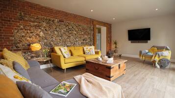 A living room with a yellow sofa, a grey sofa, a wooden coffee table, and a stone wall.