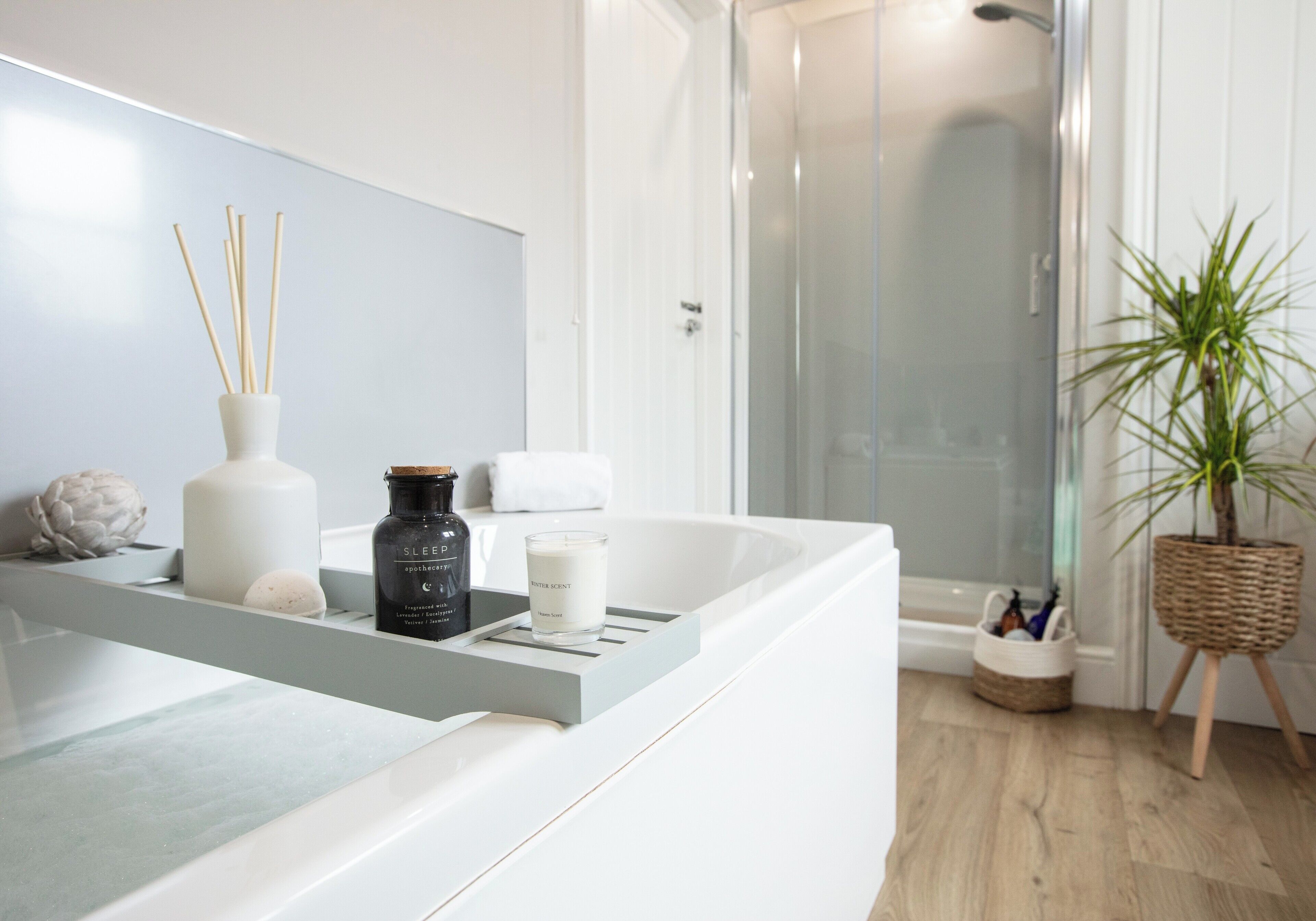 A bathroom with a white bathtub, a shower, and a plant.