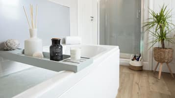 A bathroom with a white bathtub, a shower, and a plant.