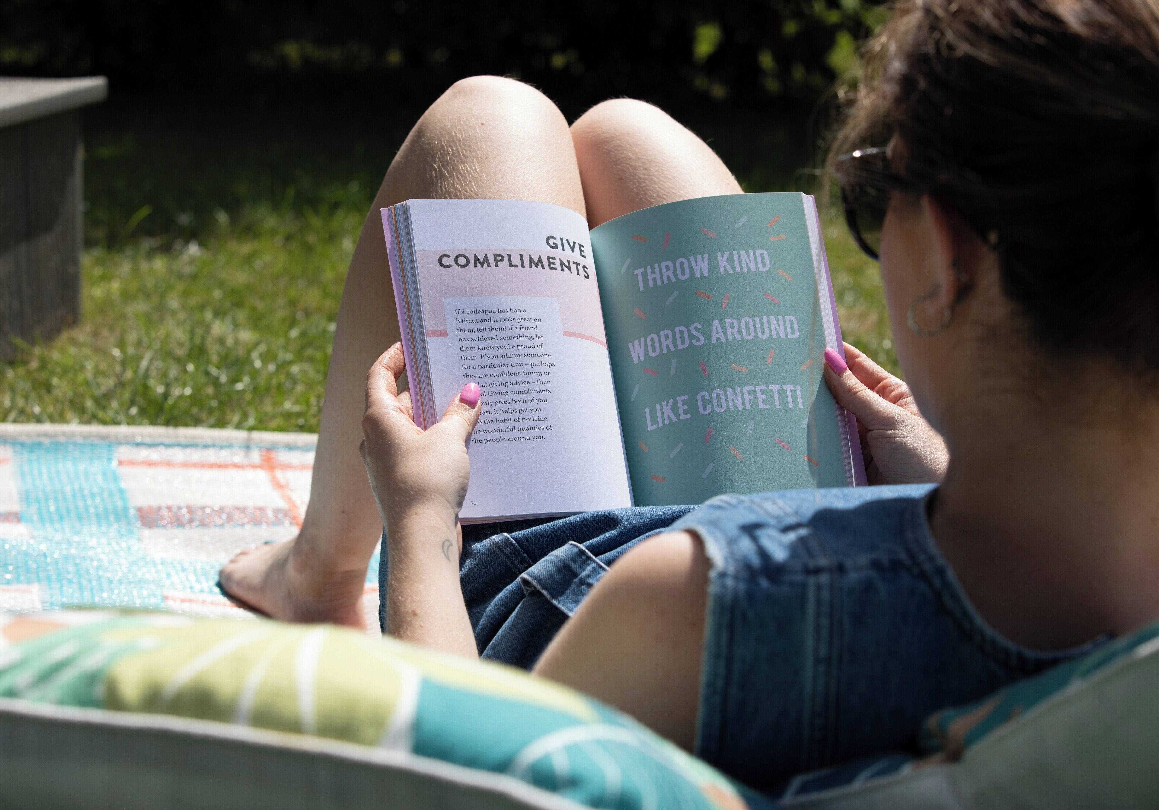 A person reading a book outdoors with a pool in the background.