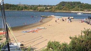 Une plage où plusieurs petits bateaux sont alignés sur le sable, un mur de pierre séparant la plage de l’eau, et quelques personnes se promenant le long du rivage.
