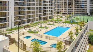A multi-story hotel with a rooftop pool area, including a main pool, smaller pools, and a tennis court.