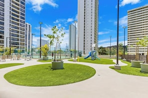 Un parco urbano moderno con prati verdi, strutture giochi e alti edifici residenziali.