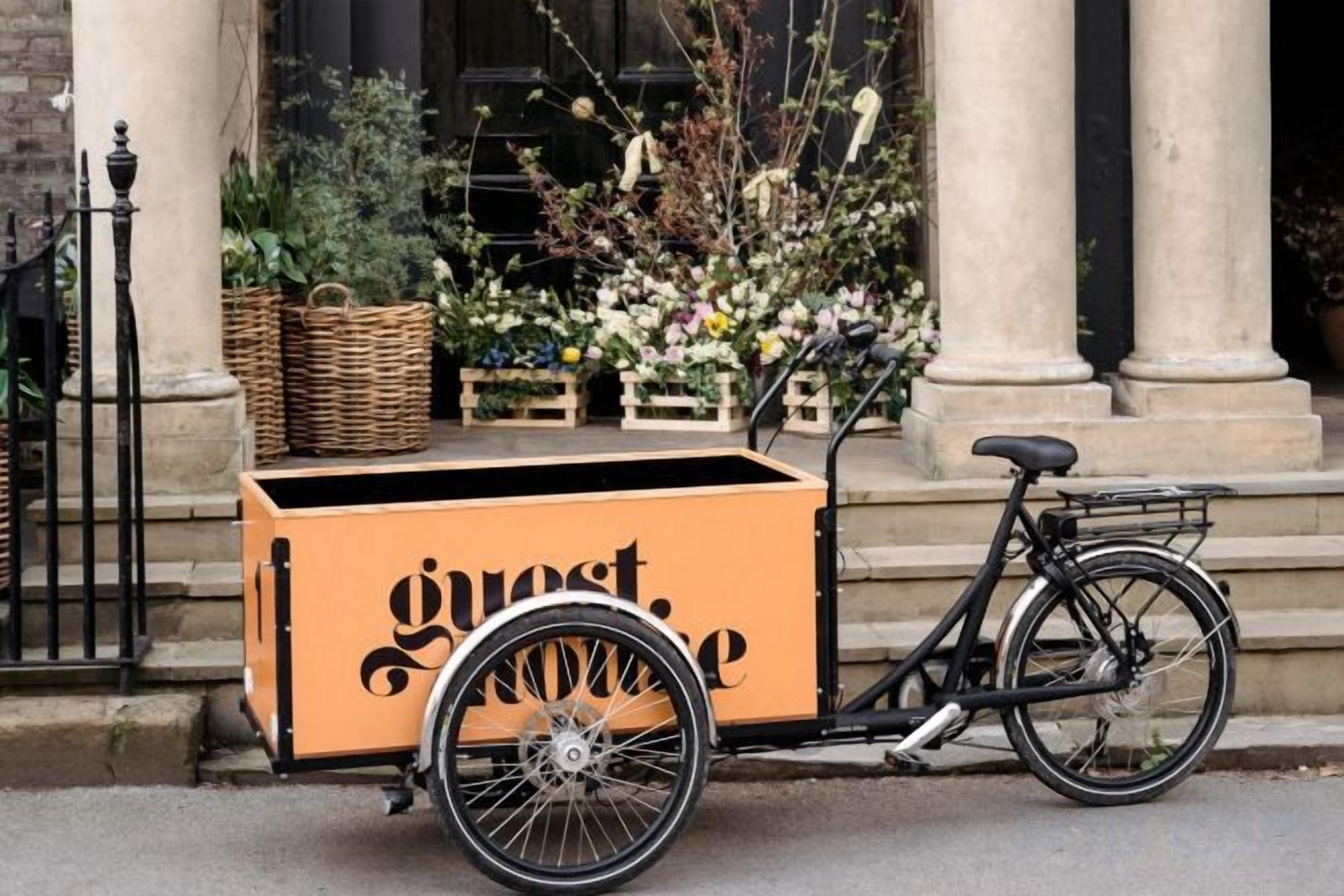 Een fiets met een bak waarin 'gast' staat, geparkeerd op een straat.
