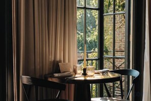 Une table avec un menu, un verre et une bougie, placée près d’une fenêtre ornée de rideaux.