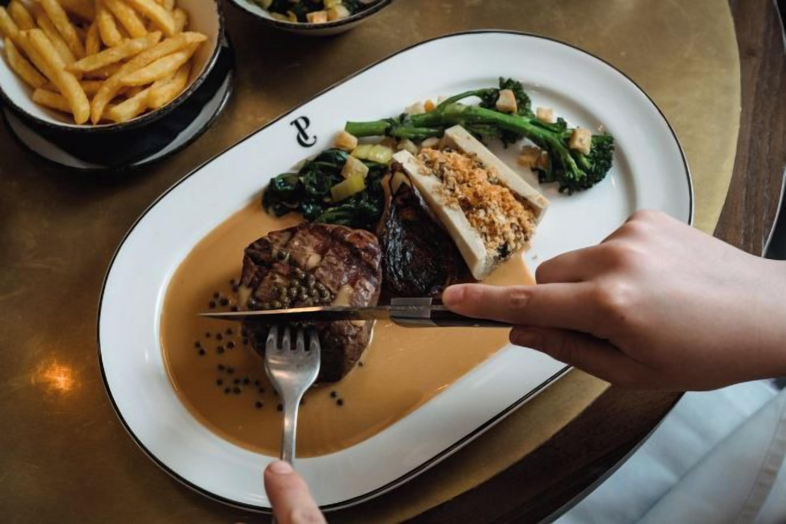 A plate with steak, vegetables, and fries on a table.