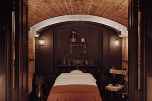 Quarto com cama, parede escura, luminária pendente e prateleira com objetos.