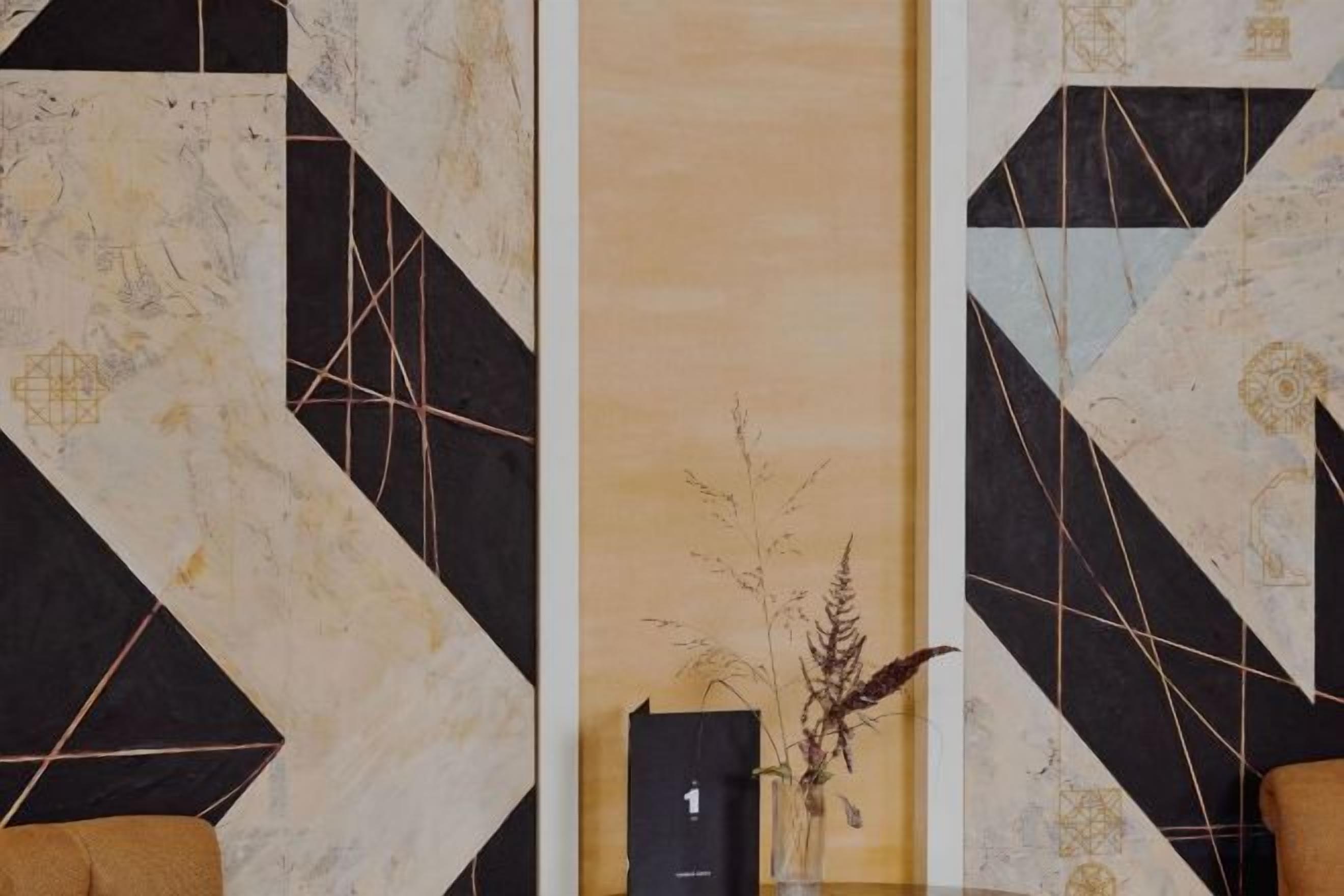 A lobby with a geometric patterned wall, a reception desk, and a vase with dried plants.