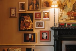 Une pièce avec une cheminée, des œuvres d’art encadrées et une lampe.