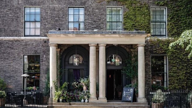 Un edificio con fachada de piedra, ventanas arqueadas y una entrada clásica con columnas.