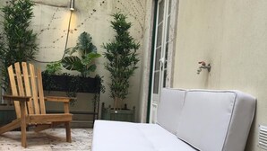 Un espacio al aire libre acogedor con un sofá blanco, una silla de madera y una pequeña mesa con un vaso y un plato.