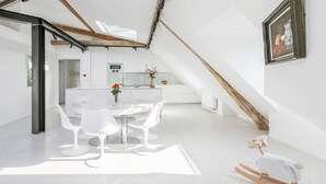 A modern kitchen with white cabinets, a central island, and a dining area with white chairs. - A STRIKING SUNLIT HAUSSMANN PENTHOUSE- LUXURY LIVING IN MONCEAU CHAMPS ELYSEES (Paris)
