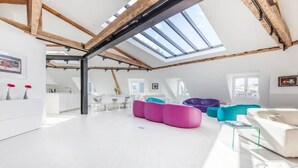 A spacious loft with a high ceiling, skylights, a white sofa, colorful bean bags, and a kitchen area. - A STRIKING SUNLIT HAUSSMANN PENTHOUSE- LUXURY LIVING IN MONCEAU CHAMPS ELYSEES (Paris)