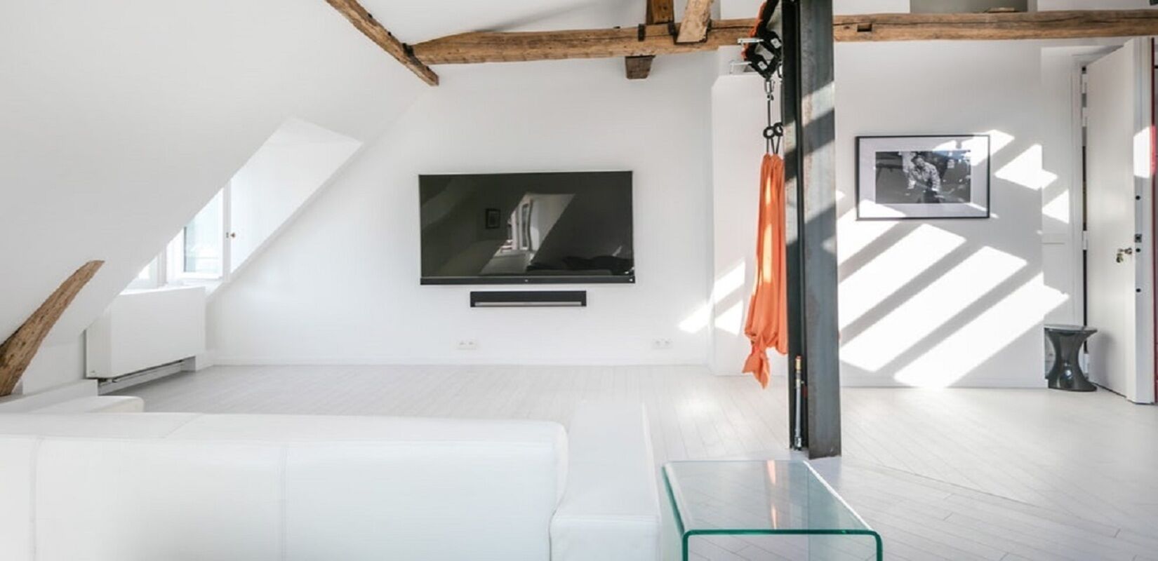 A modern living room with a flat-screen TV mounted on the wall, a glass coffee table, and a white sofa.