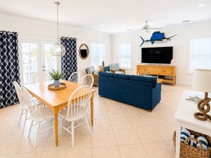 A modern living room with a dining area, a blue sofa, a TV, and a ceiling fan.