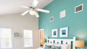 Une chambre à coucher comprenant un lit, un banc, un ventilateur de plafond et une table de chevet avec une lampe.